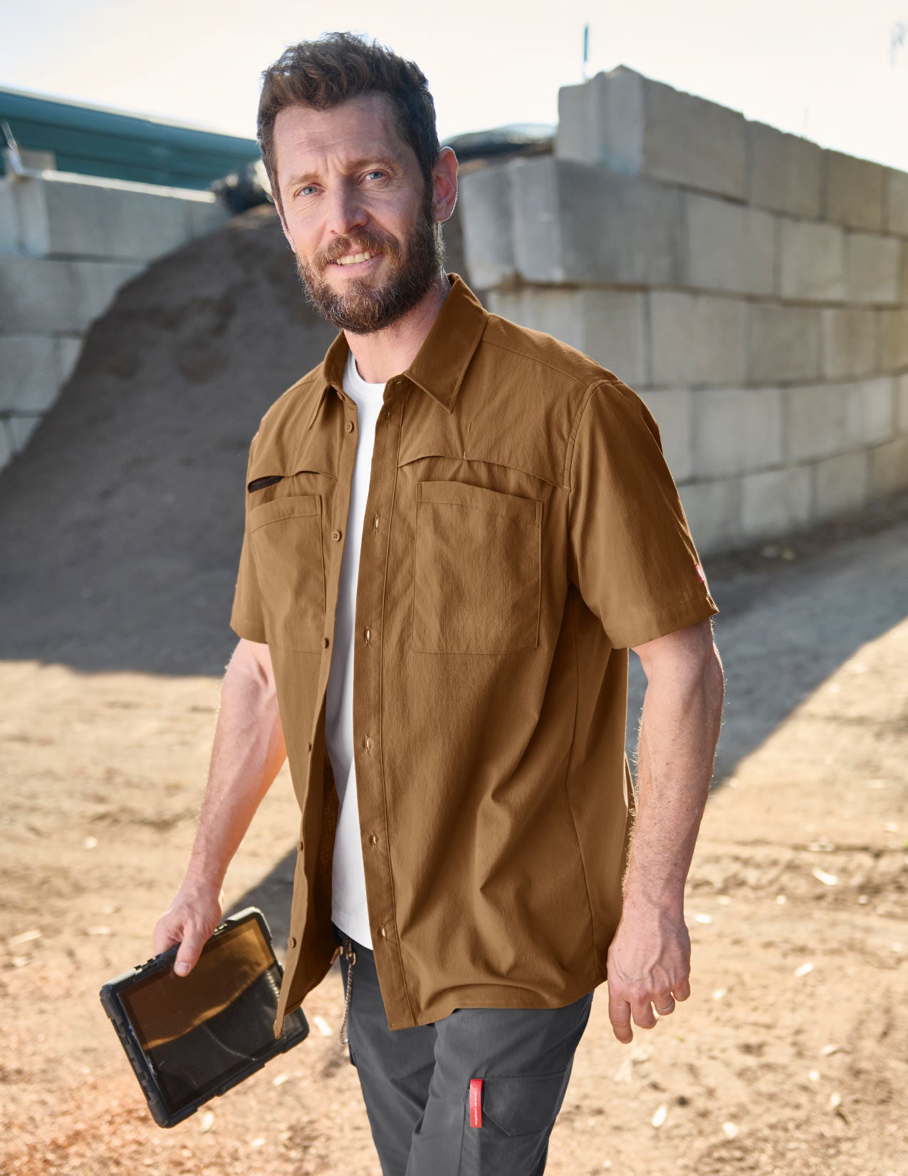 Man wearing an open brown work shirt, a tablet in his hand