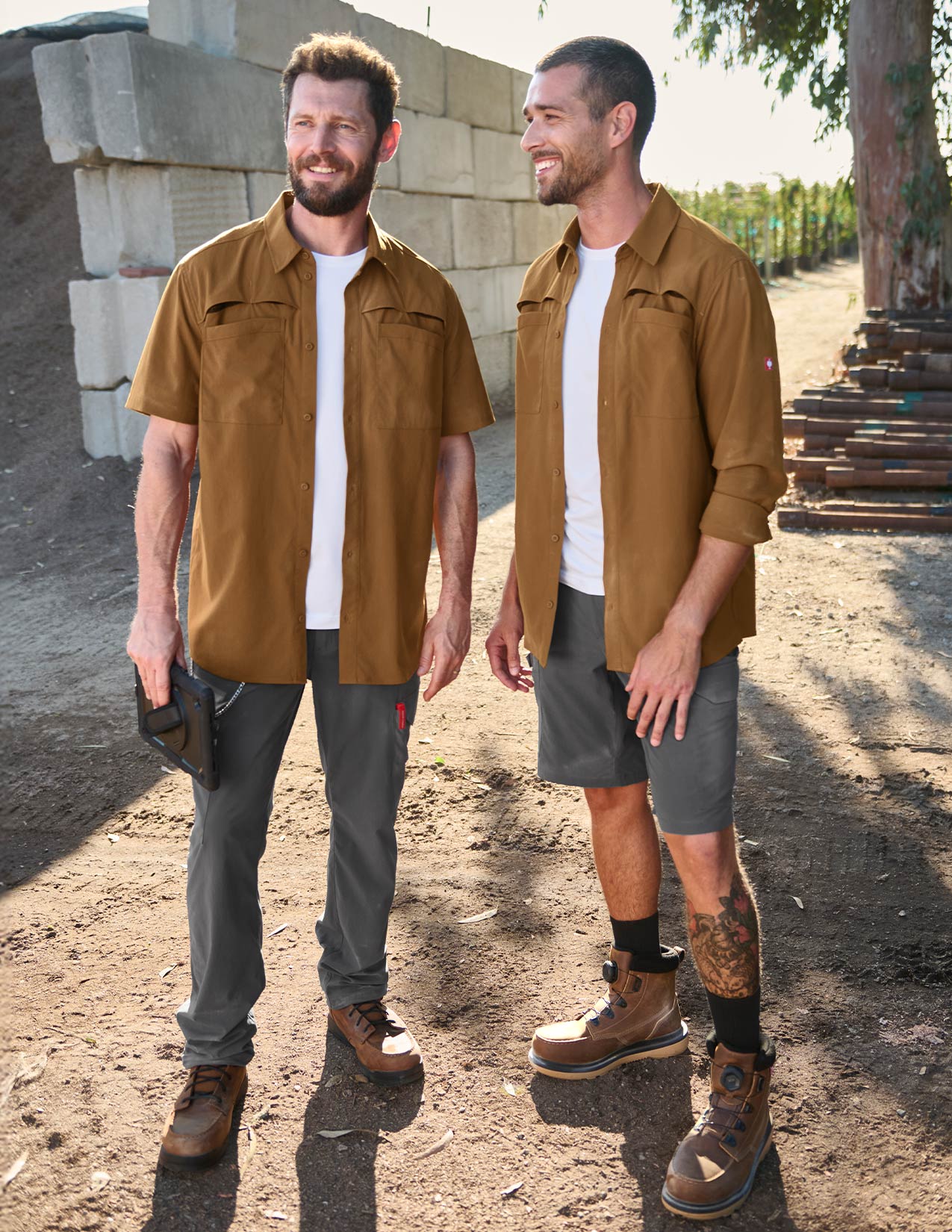 Two men in brown work shirts and grey pants, one with a tablet in his hand