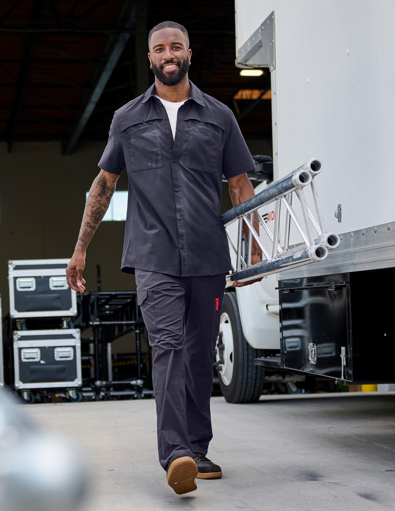 Man in a dark blue work shirt und pants walking while holding a metallic object