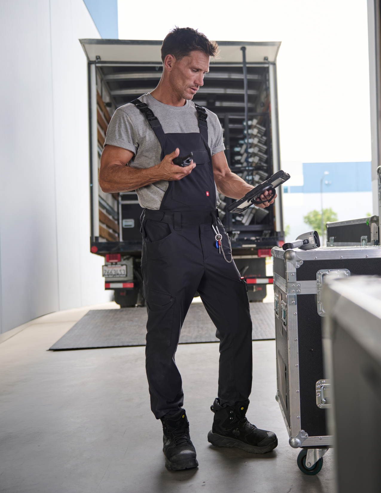 A man wearing gray bibs, looking down at his tablet