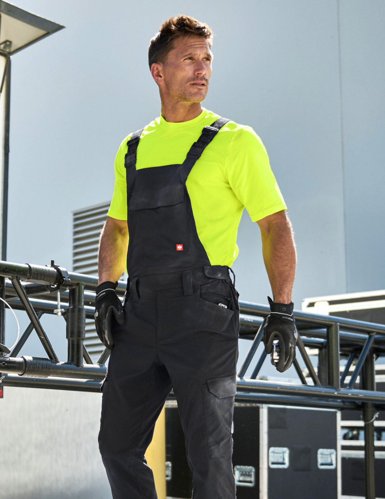 Person wearing a high-visibility shirt and black overalls on a construction site.