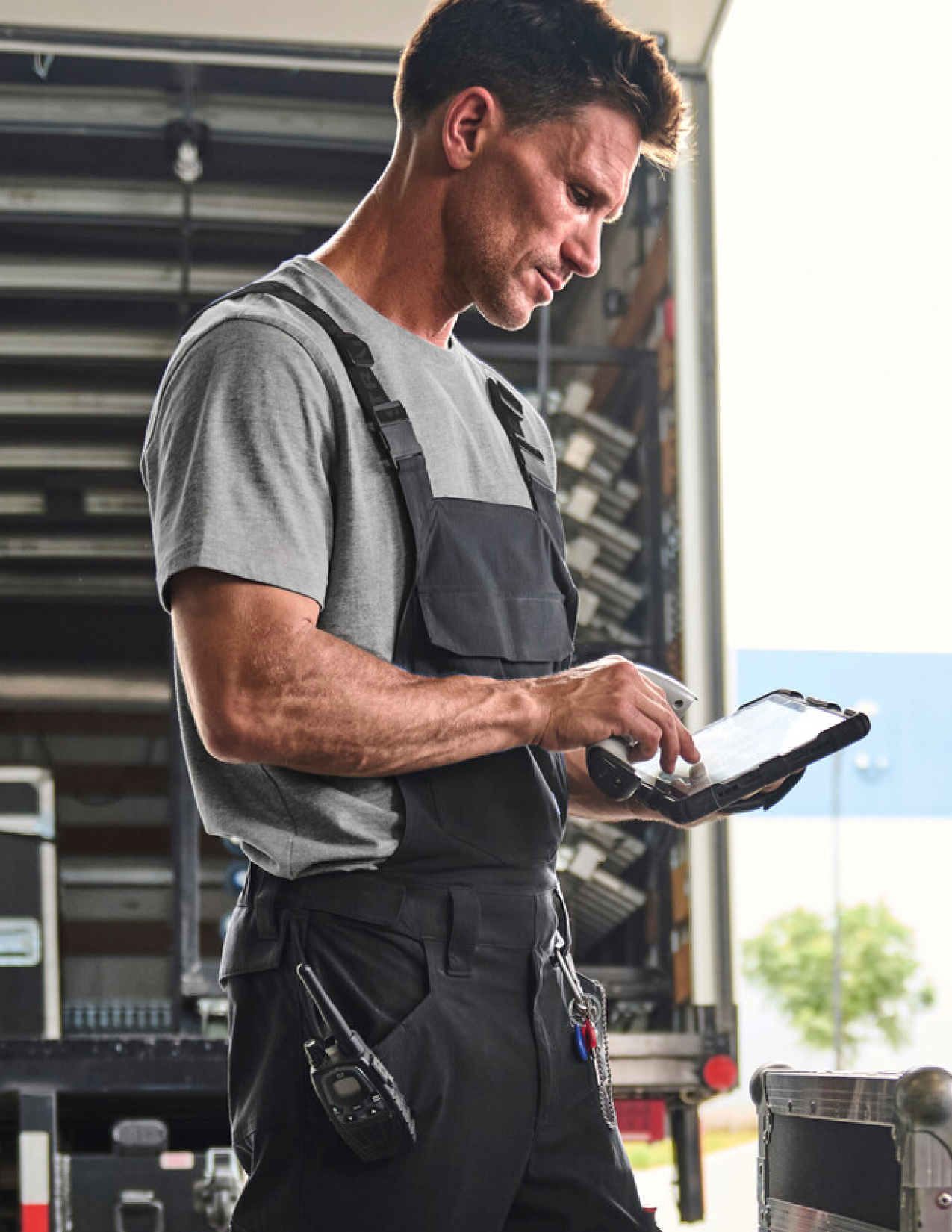 Mechanic using a tablet in a garage setting wearing black bib overalls