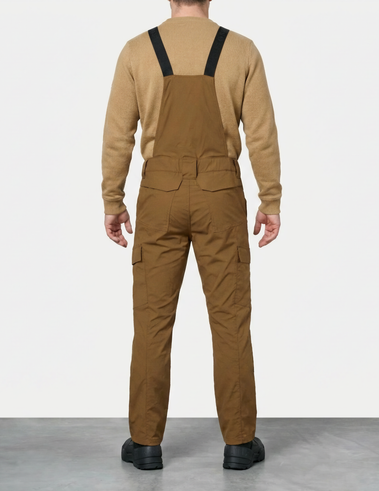Person wearing brown bib overalls and a matching sweater on a white background