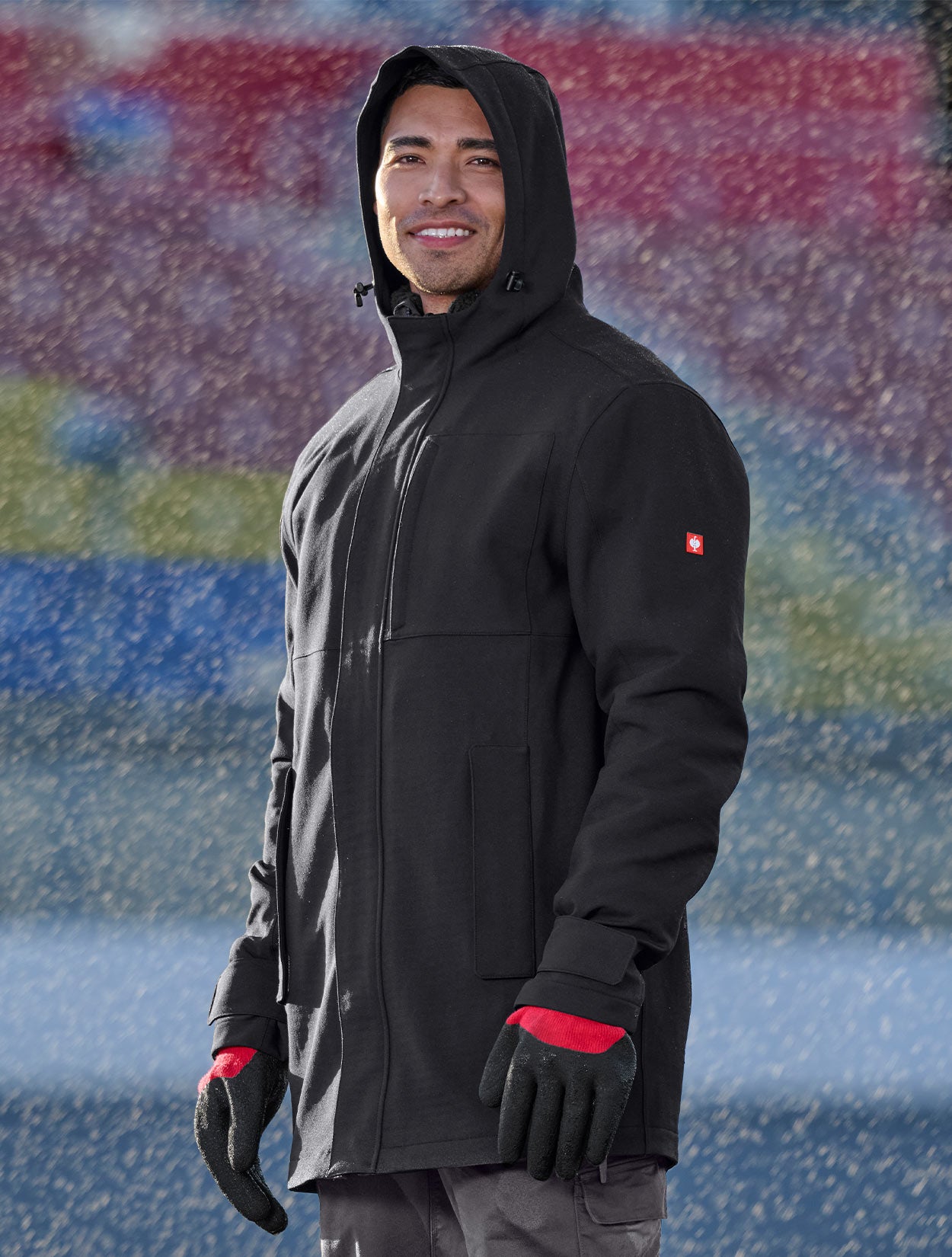 Person wearing a black jacket and gloves standing in front of a colorful abstract background