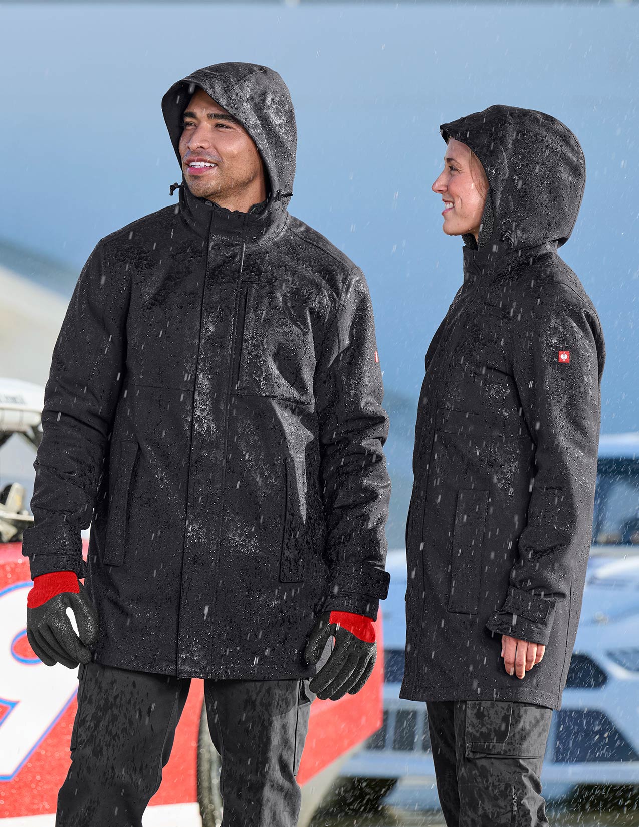 Two people wearing black rain coats standing in a rainy environment.