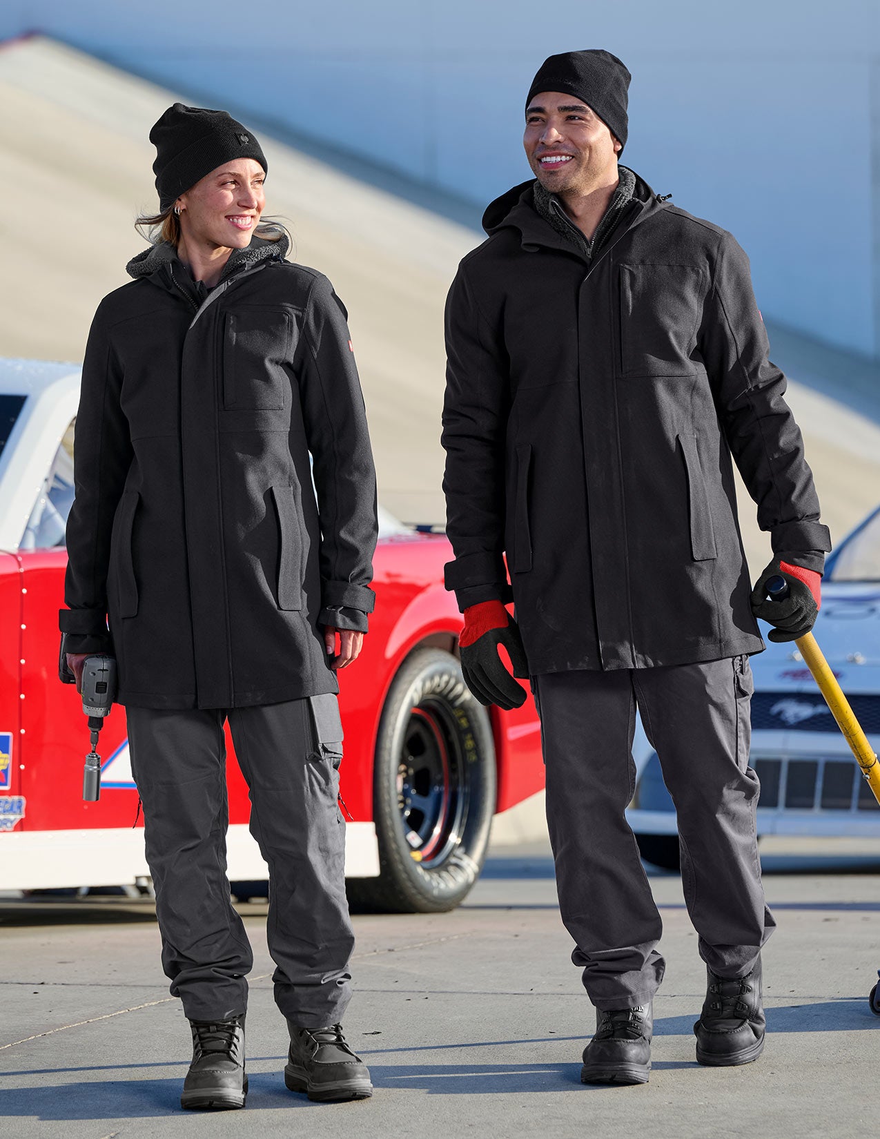 Two people wearing black rain coats and hats standing in front of a red vehicle.