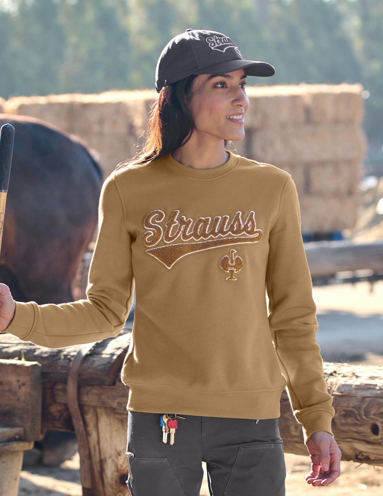 Person wearing a sweatshirt with 'Strauss' logo, standing outdoors with hay bales in the background.