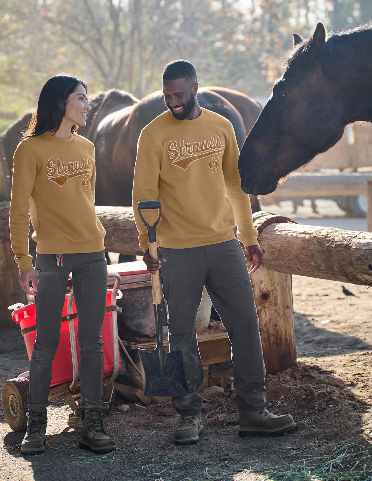 Two people wearing brown sweatshirts with a horse in the background at a farm.