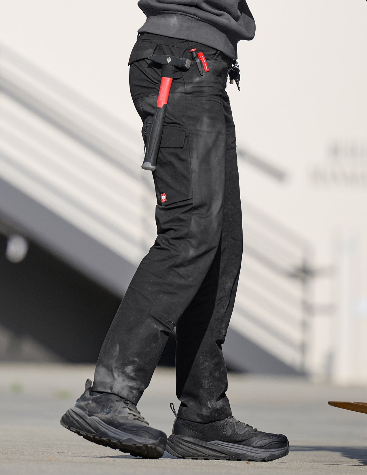 Person wearing black tactical pants with red accents and black shoes on a blurred background