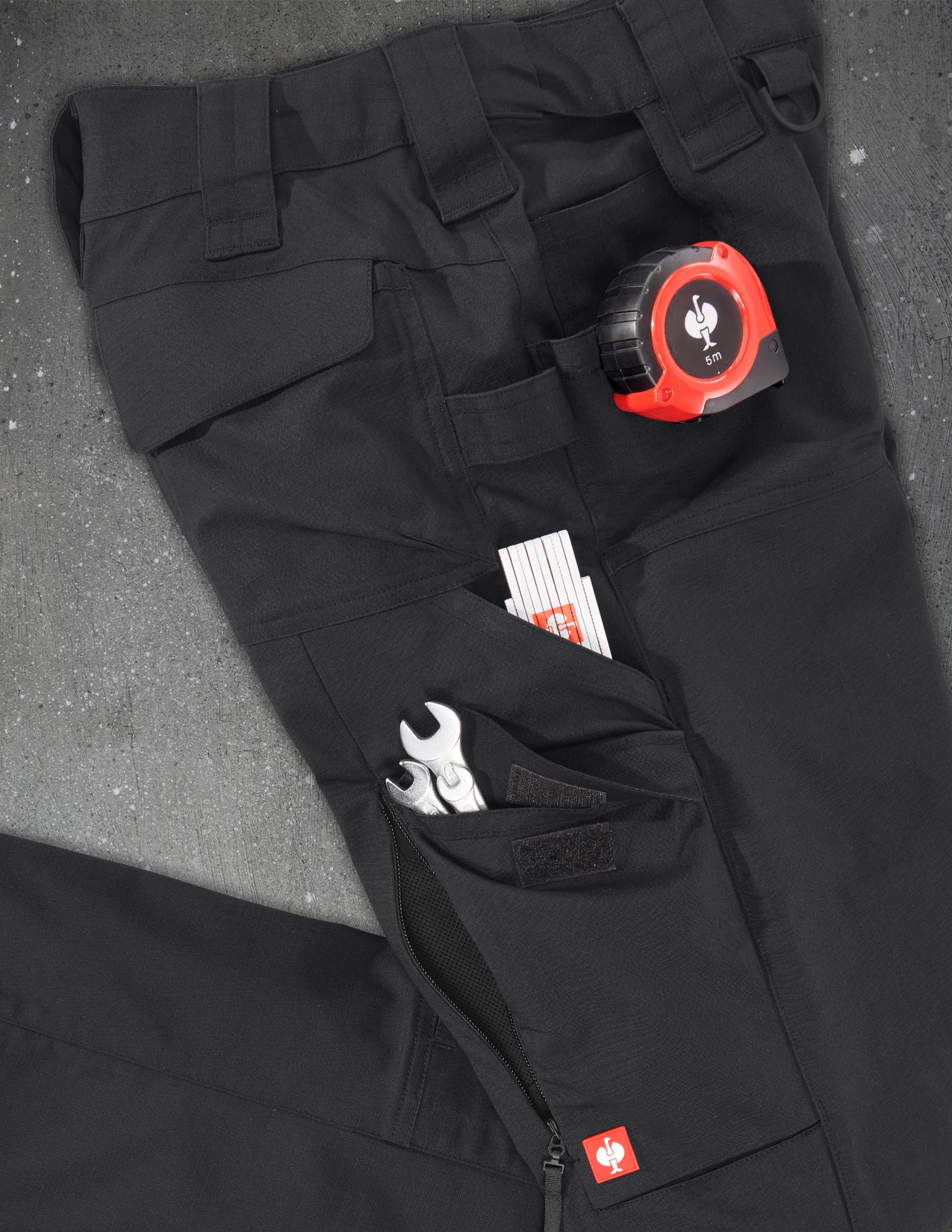 Black work pants with tools and a tape measure in pockets on a gray surface