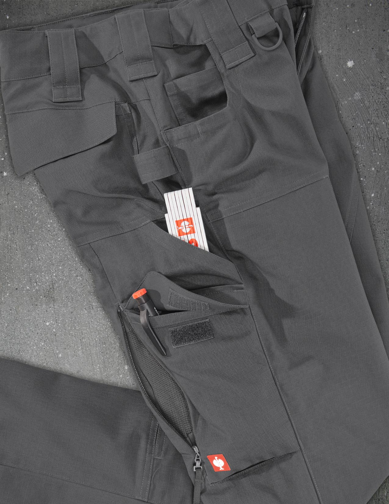 Dark gray tactical pants with multiple pockets and visible branding on a gray surface