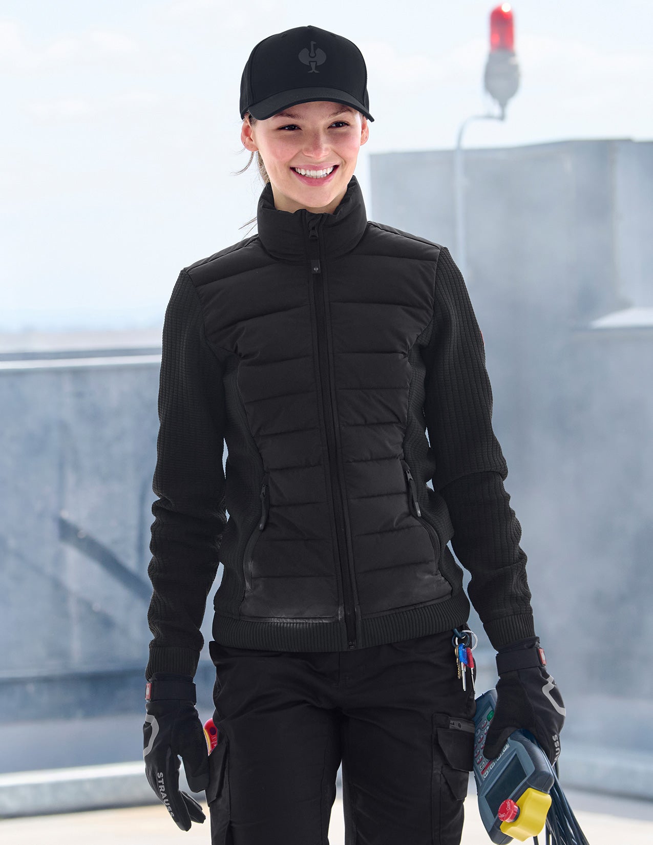 Person wearing a black puffer jacket and gloves standing on a rooftop.