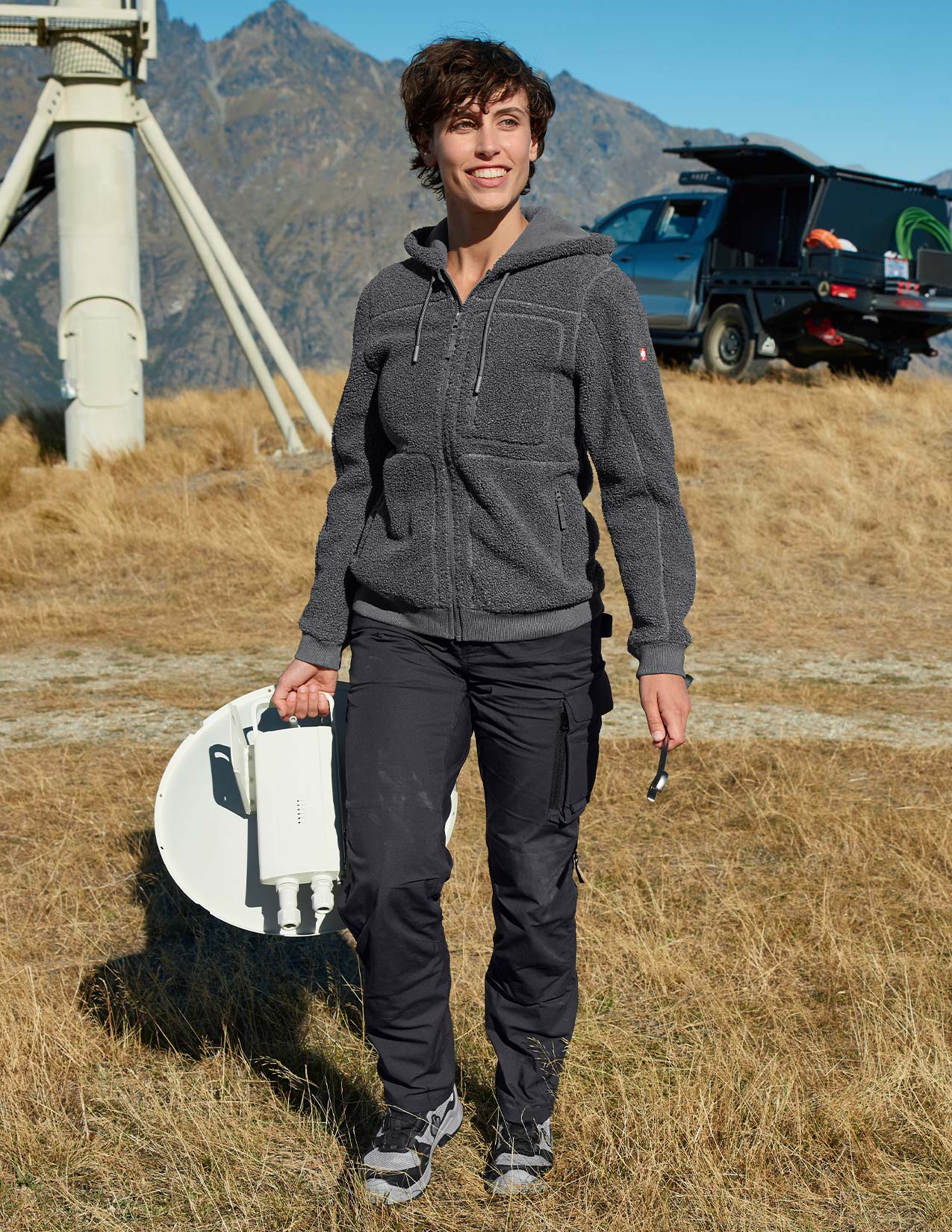 Person holding a satellite dish in a mountainous area with a truck in the background