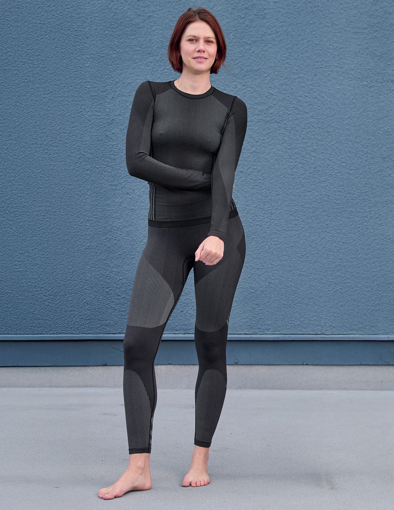 Person wearing a black and gray thermal pants and longsleeve against a blue wall.