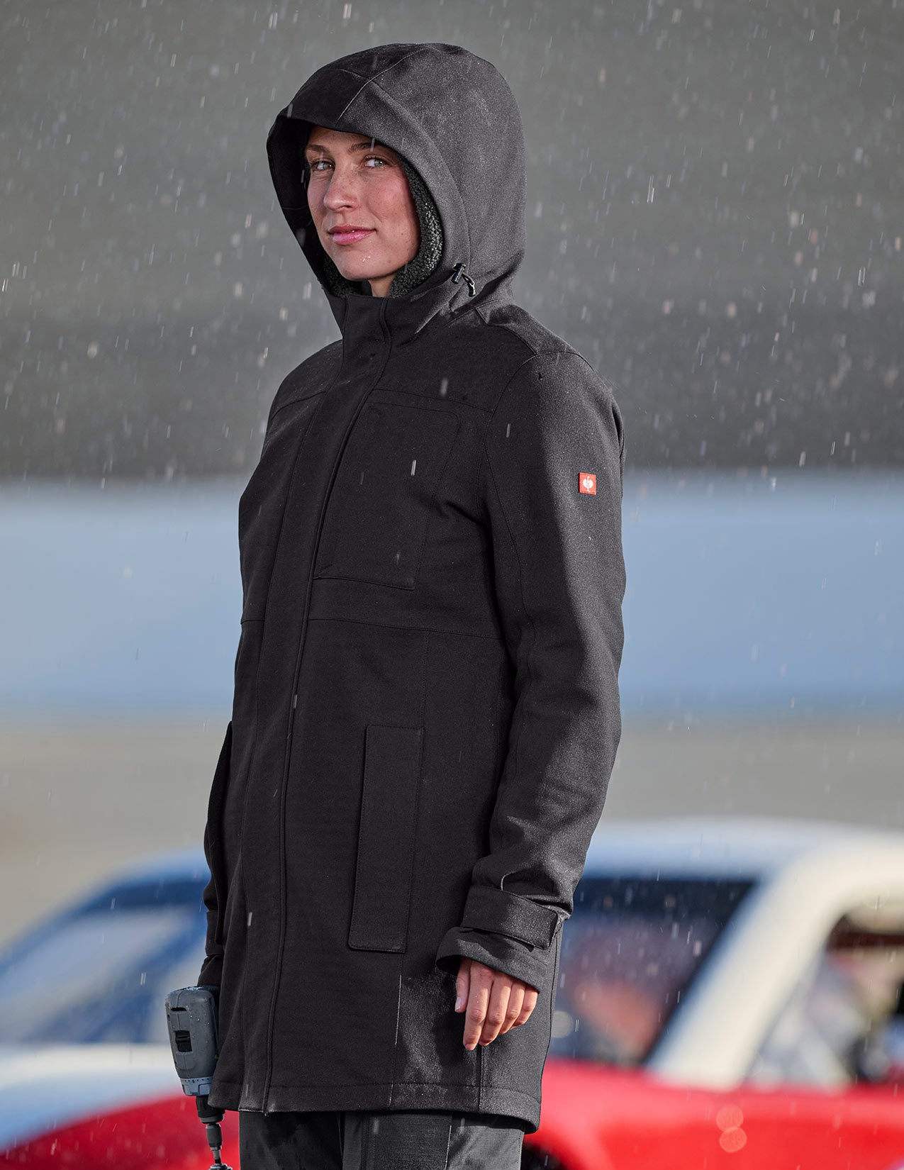 Woman wearing a black raincoat with a hood in a rainy outdoor setting
