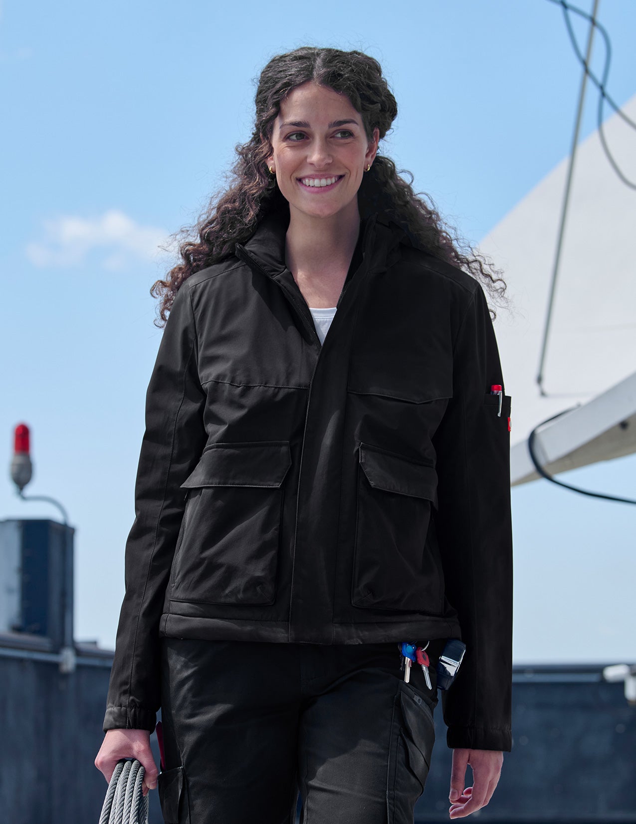 Woman wearing a black jacket on a rooftop with a clear sky background.