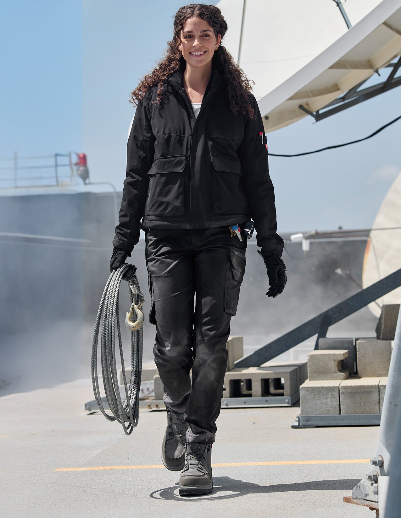 Woman in black work attire walking on a rooftop with tools.