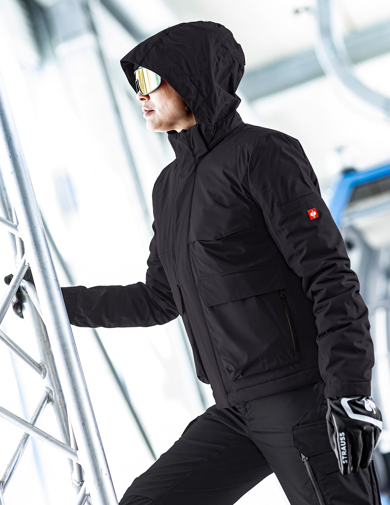 Person wearing a black winter jacket with a hood in an indoor setting.