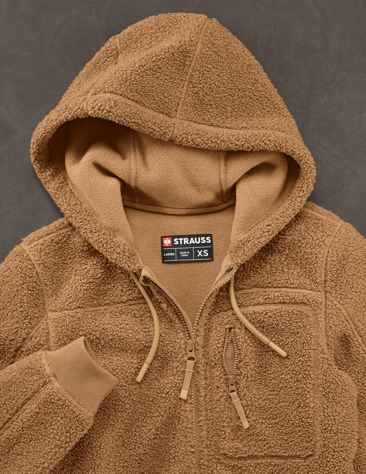 Brown fleece jacket with a visible Strauss label on a dark background