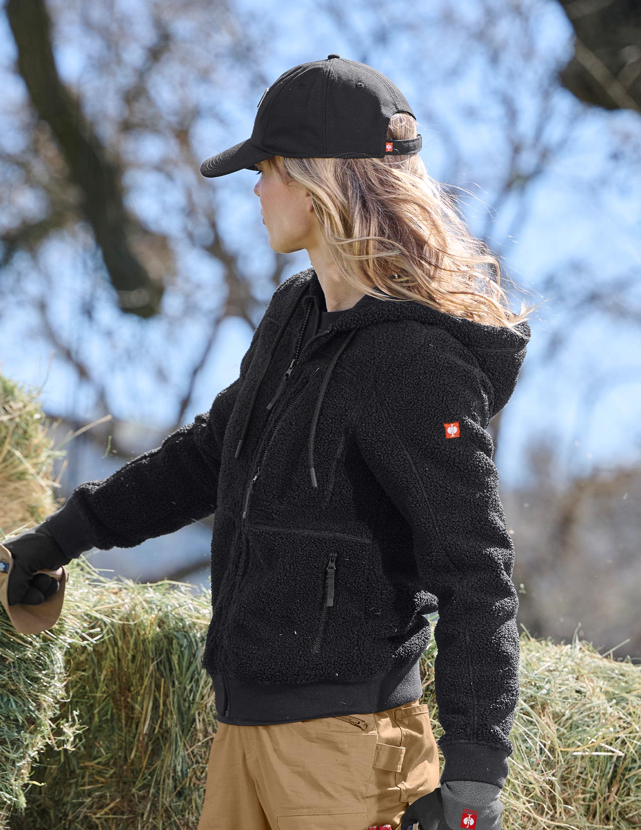 Person wearing a black hoodie and cap standing near hay bales outdoors