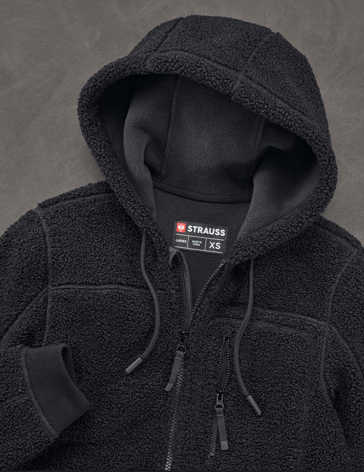 Black fleece jacket with a visible Strauss label on a gray background