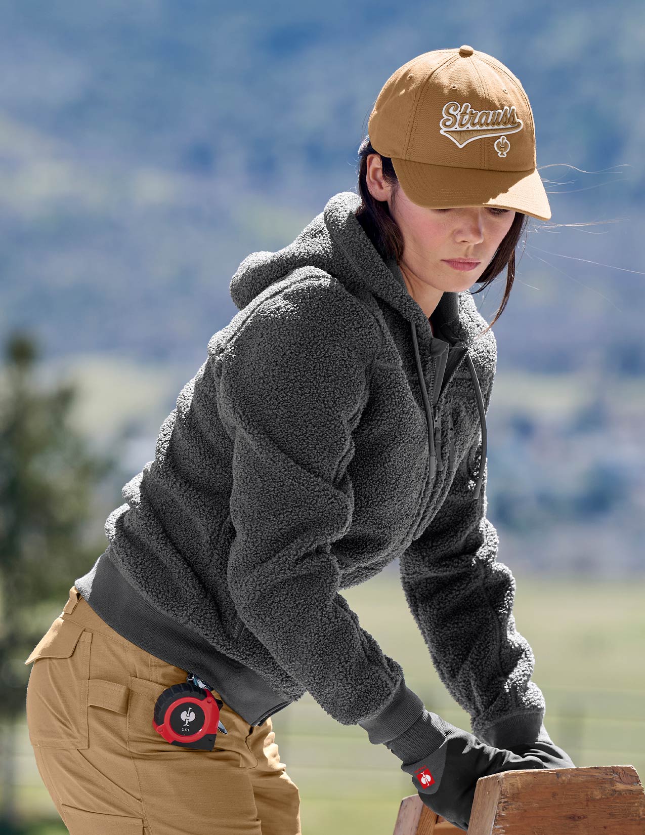 Women wearing a brown cap and gray jacket outdoors with mountains in the background