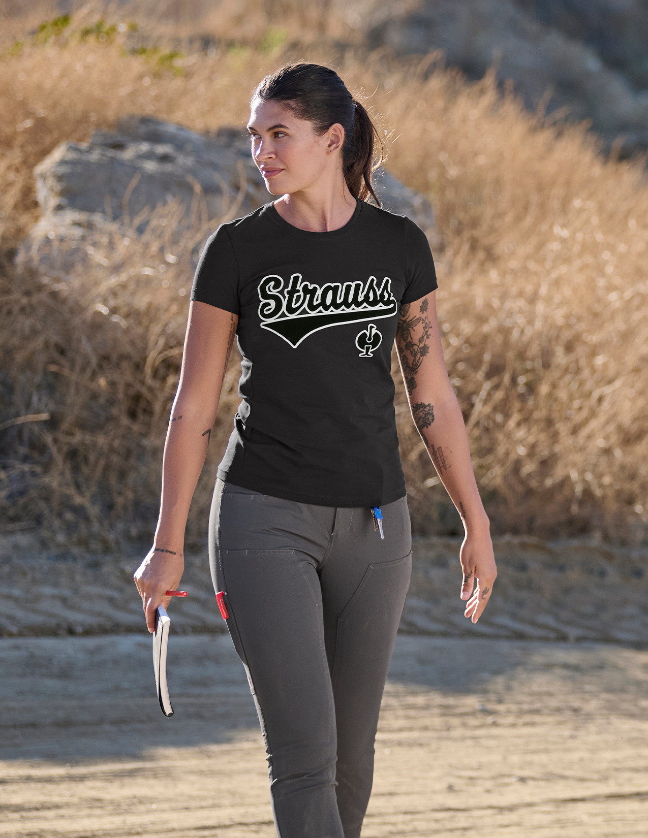 Woman walking outdoors wearing a black t-shirt with 'Strauss' logo
