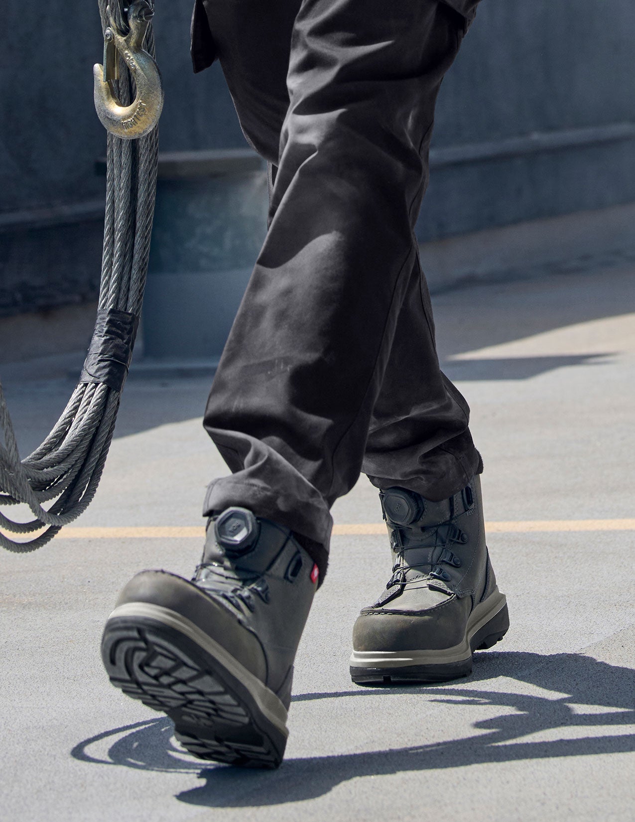 Person wearing carbongrey boots and pants with a hook and rope in the background