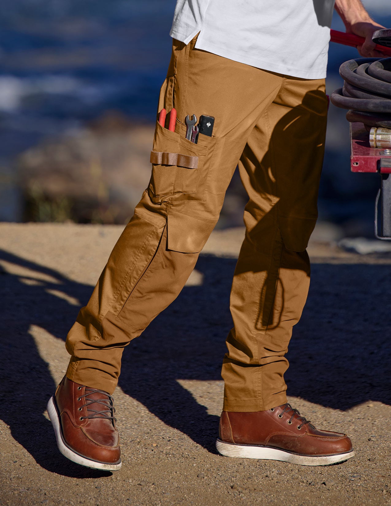 Person wearing brown cargo pants with tools in pockets by a body of water.