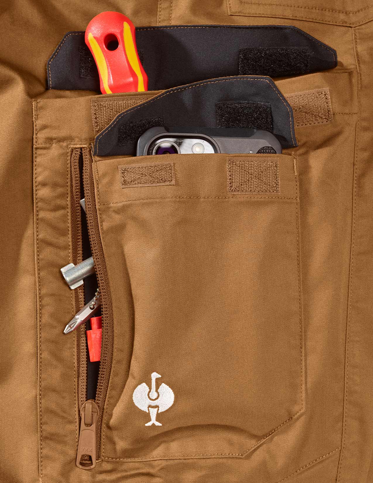 Close-up of a brown pant pocket with tools and a logo.