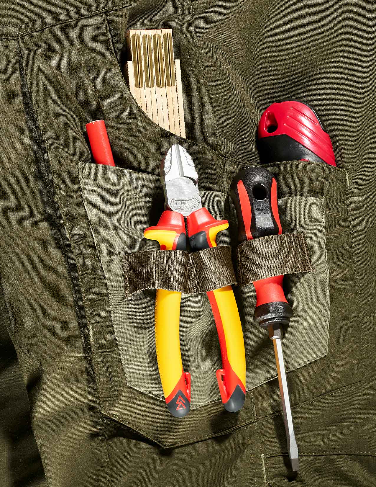 Tools including pliers and screwdriver in a pocket of green work pants.