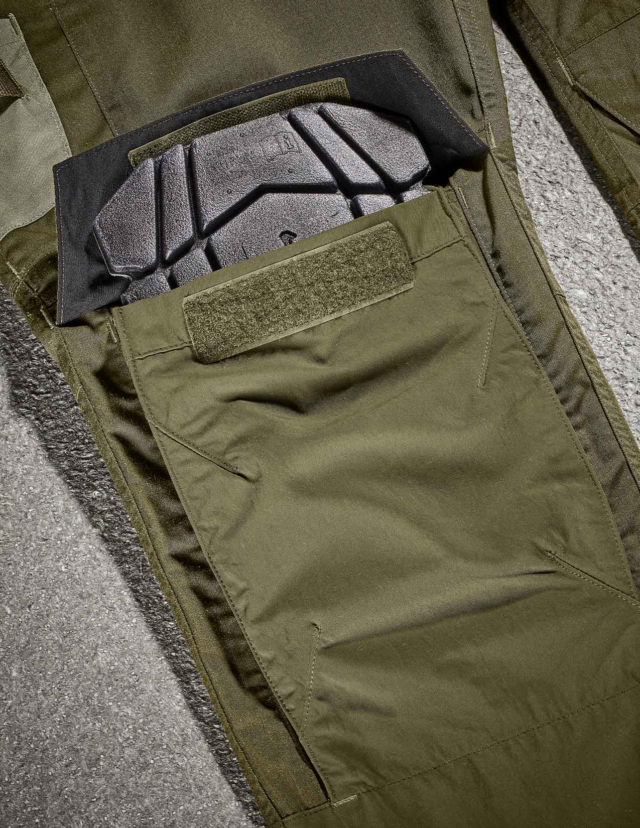 Close-up of green tactical pants with a kneepad on a gray surface