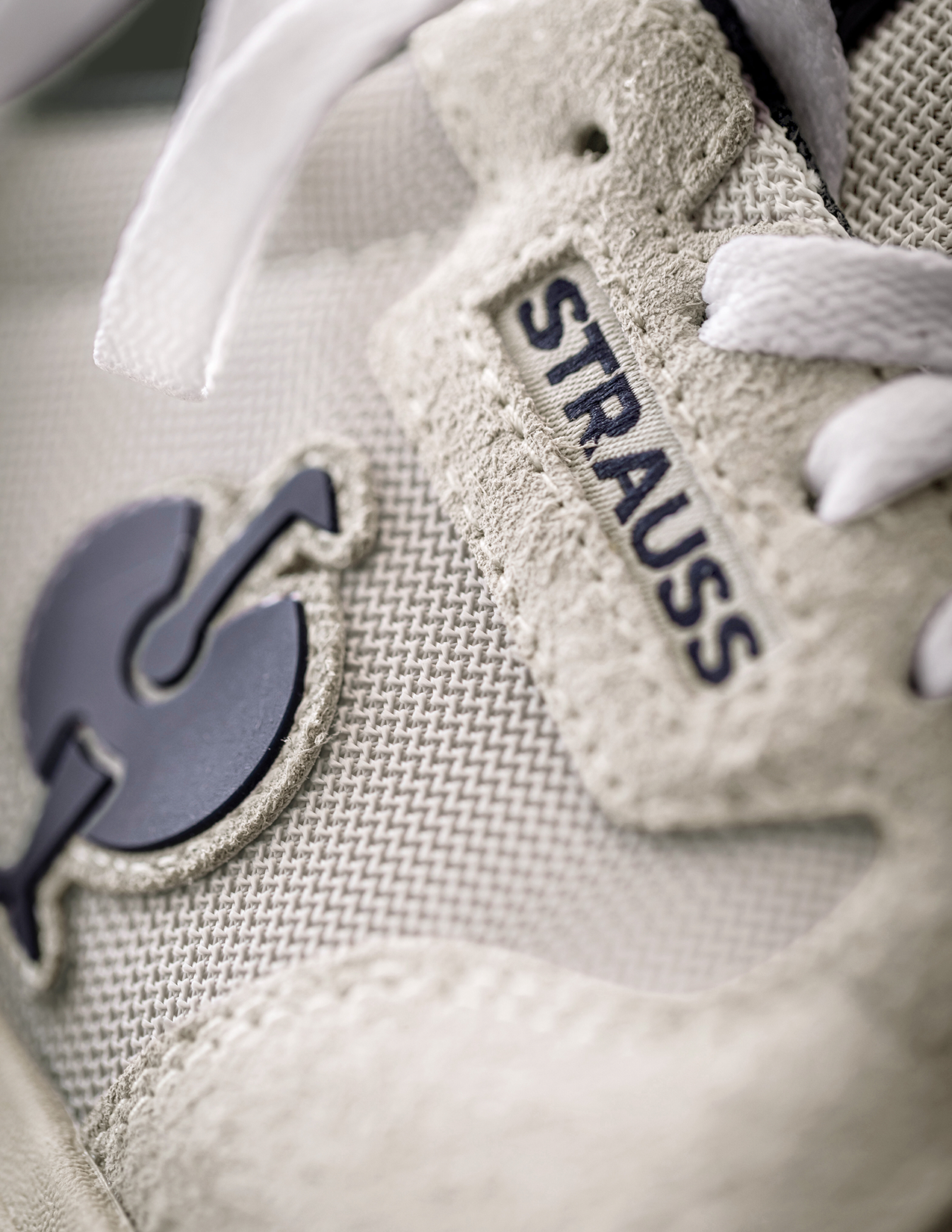 Close-up of a beige sneaker with 'Strauss' branding on a light background