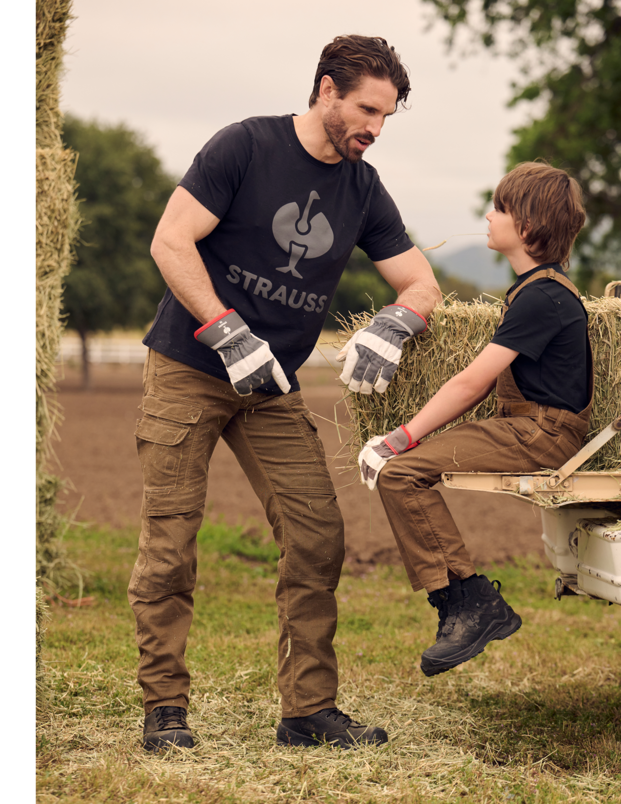 Man in brown work pants and child in outdoor setting with 'Strauss' logo visible