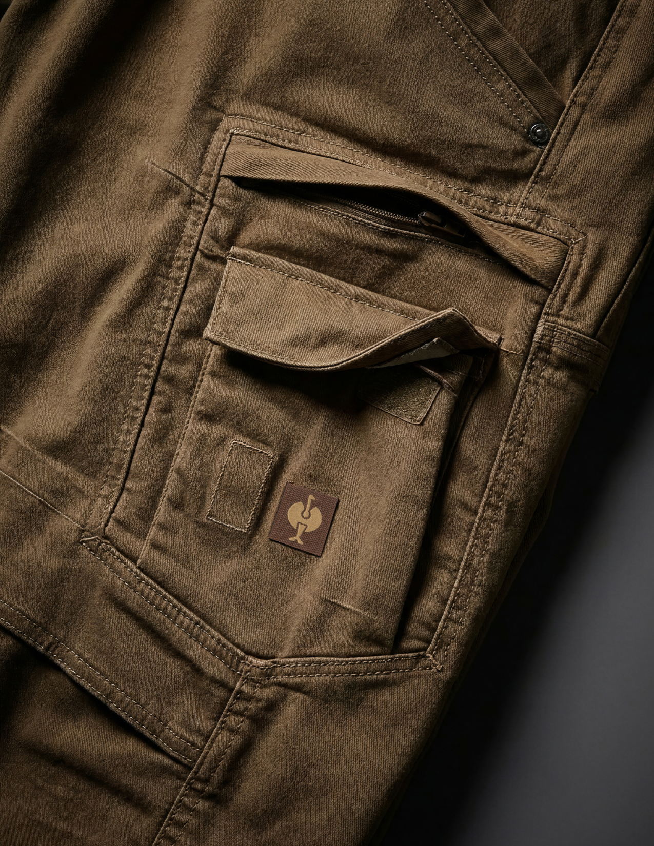 Close-up of brown pants with a brand logo on a dark background
