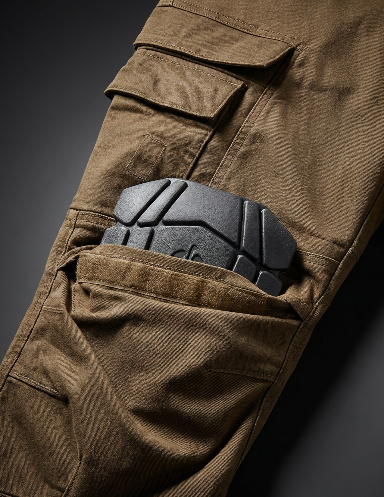 Brown pants with a black protective knee pad on a dark background