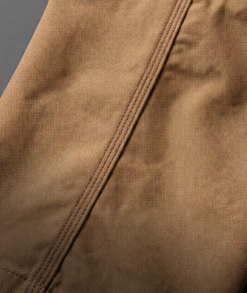 Close-up of a brown canvas or suede-like fabric surface with a diagonal stitched seam.