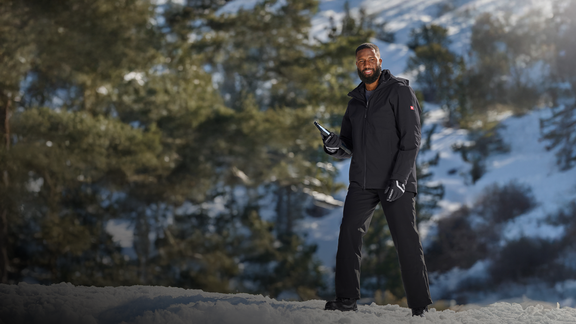 Person standing in a snowy landscape holding a device in black jacket