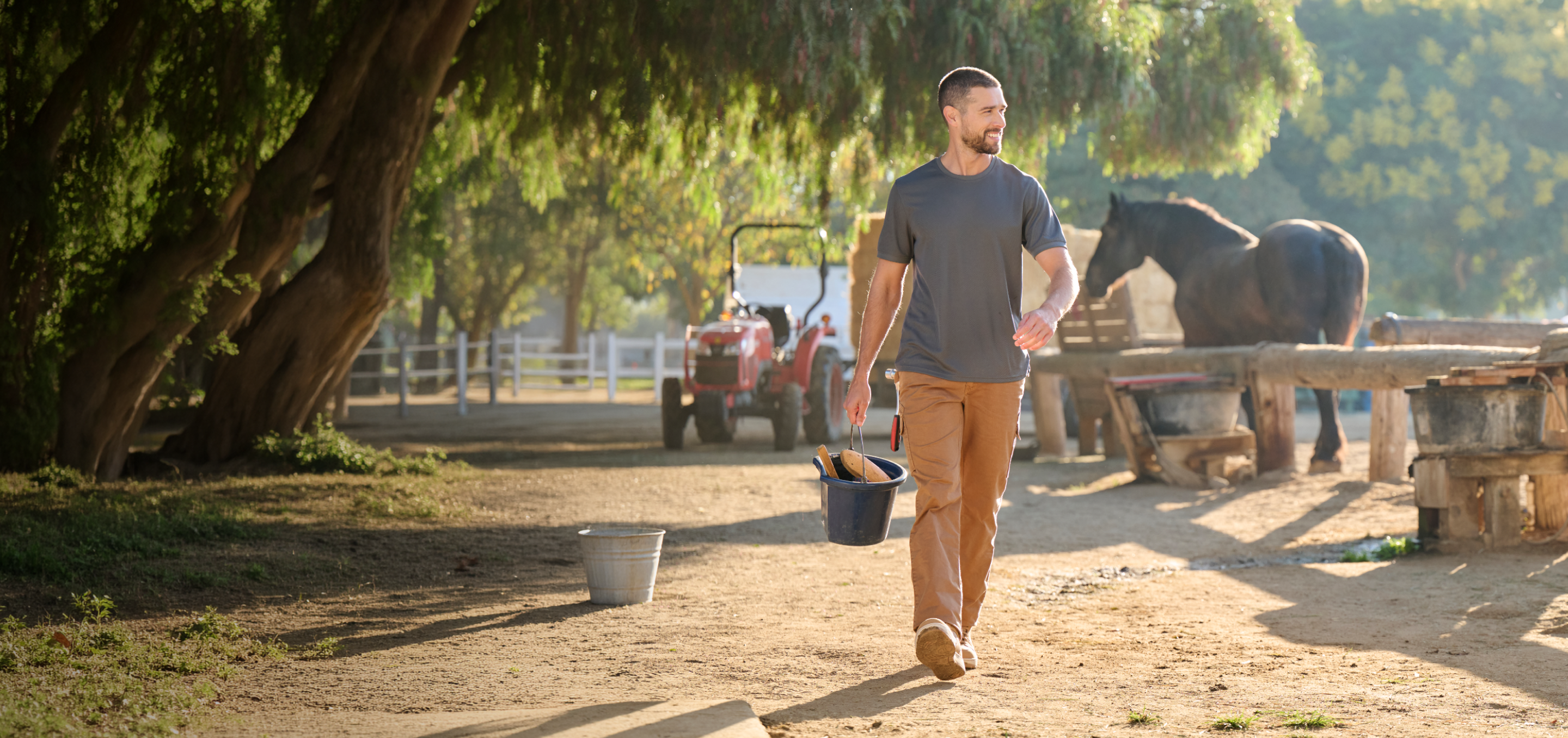 A man walking on a horse ranch with a bucket in his hands