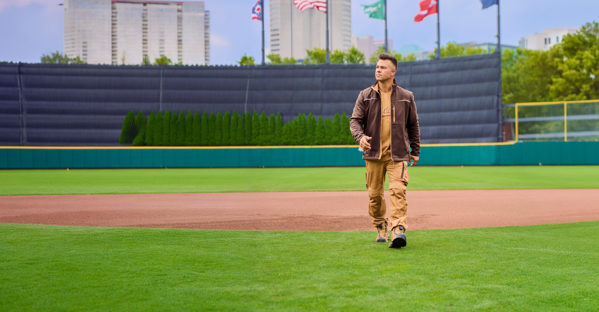 Nick Swisher walking on a baseball field wearing brown and beige STRAUSS motion 2020 workwear.