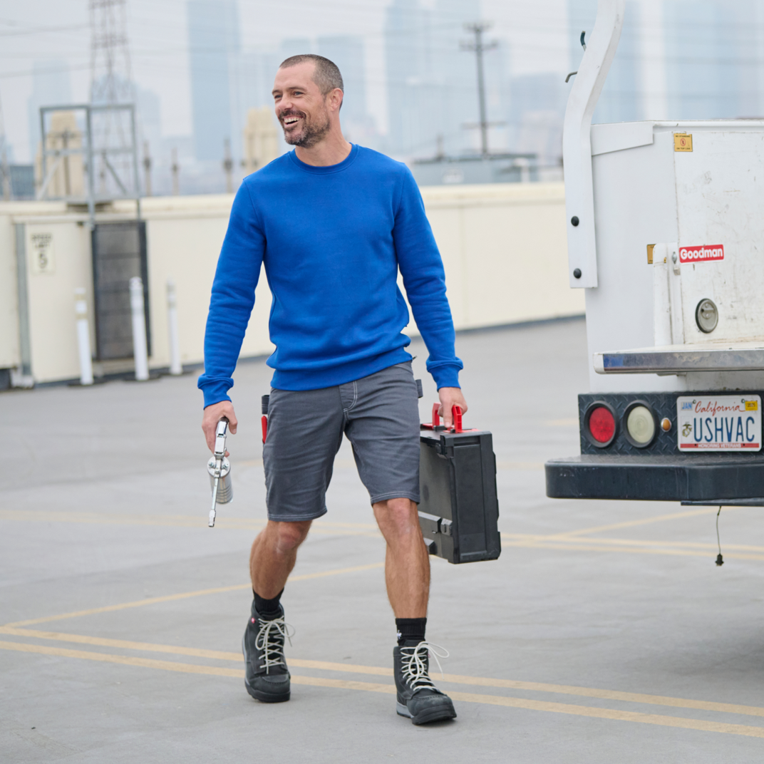 A man wearing a blue sweatshirt and gray shorts, holding a tool box in his hand