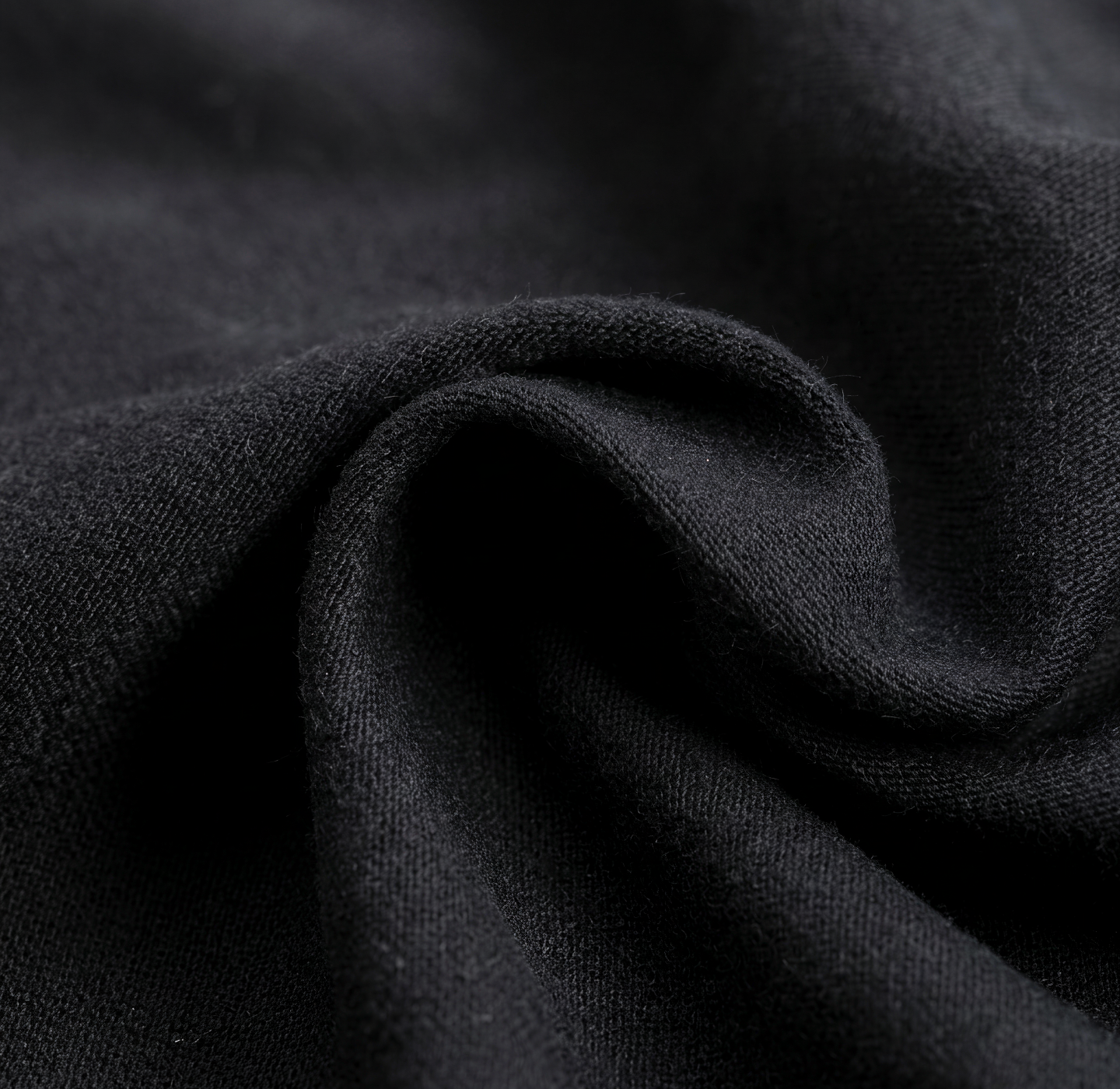 Close-up of black fabric with visible texture and gentle folds, creating soft shadows and highlights.