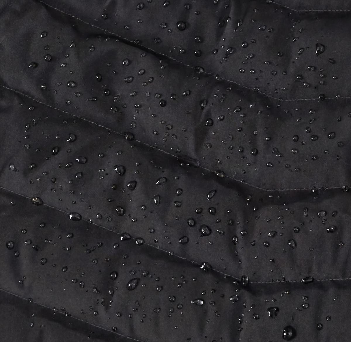 Close-up of a black, quilted fabric with water droplets scattered across its surface, showing water resistance.