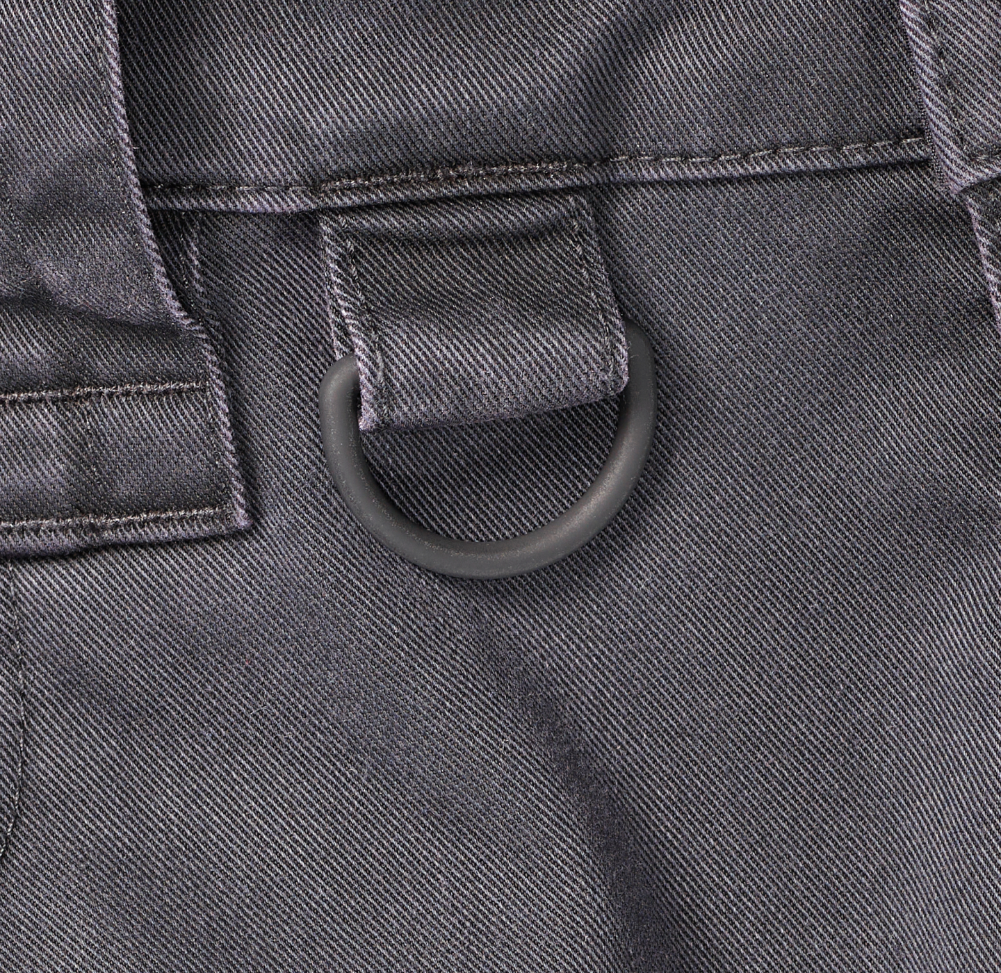 Close-up of a black fabric loop with a metal D-ring attached to a pair of dark pants, showing stitching and fabric texture.