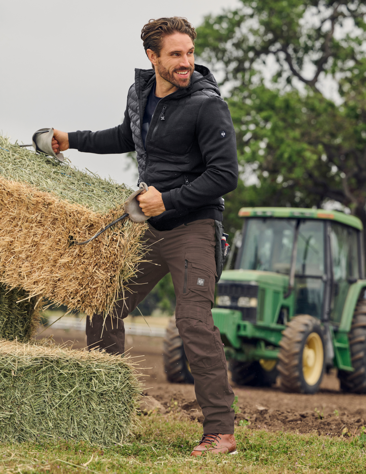 Man carrying a bundle of hay with a tractor in the background