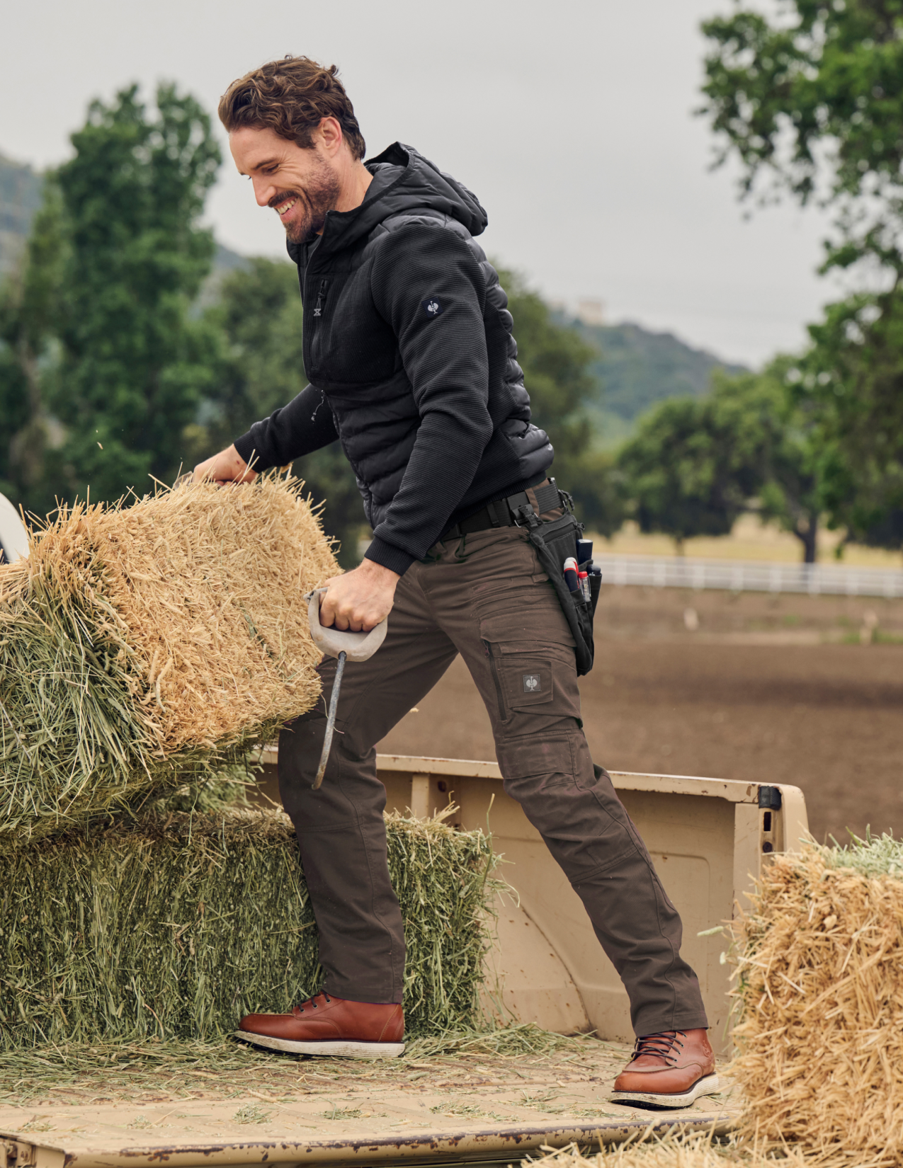 Man in outdoor setting with hay bales and trees in the background