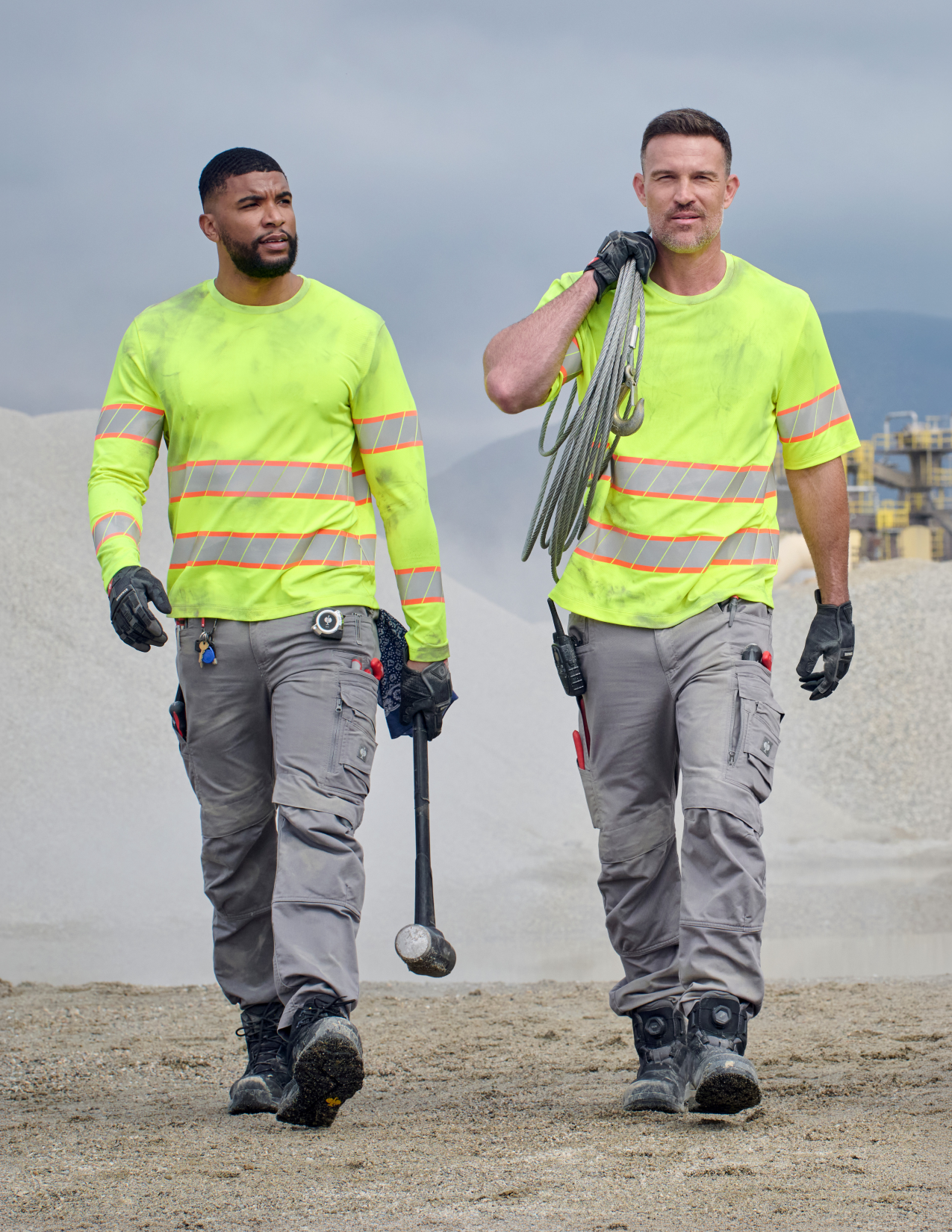 Two workers in high-visibility safety gear walking on a construction site.