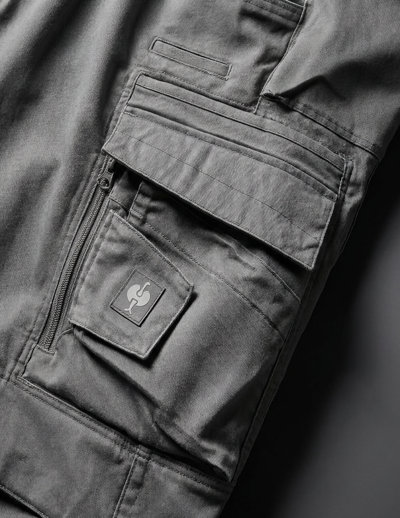 Close-up of dark grey pants with the brand logo on a black background