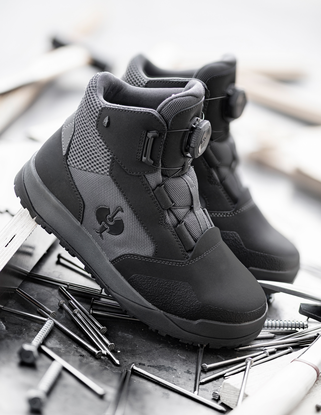 Black and gray work boot on a metallic surface with scattered nails.
