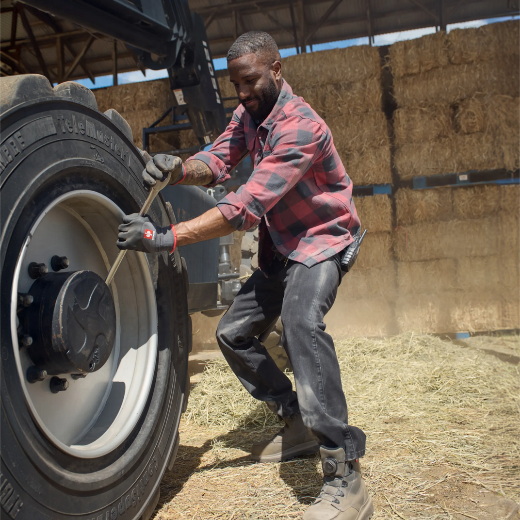 Man working on a large tire in a barn setting with hay bales.